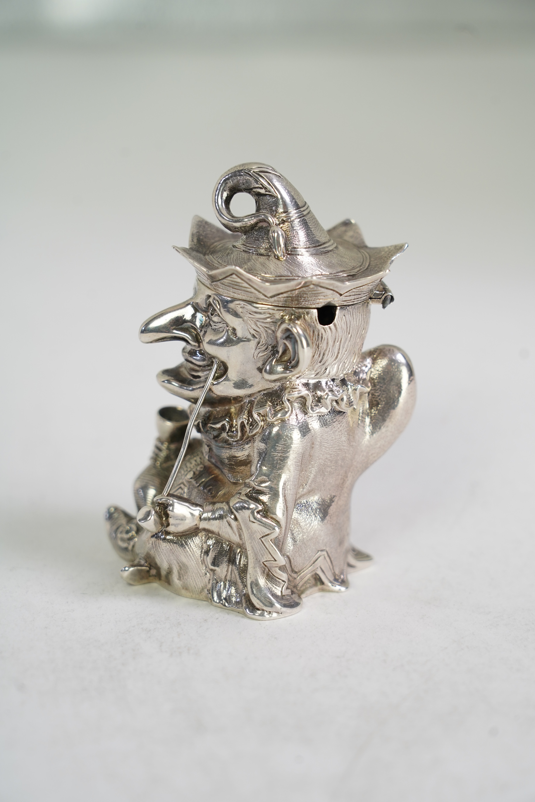 A rare Victorian novelty cast silver mustard pot, modelled as seated cross-legged Mr. Punch, holding a wine glass and smoking a pipe, by Robert Hennell III